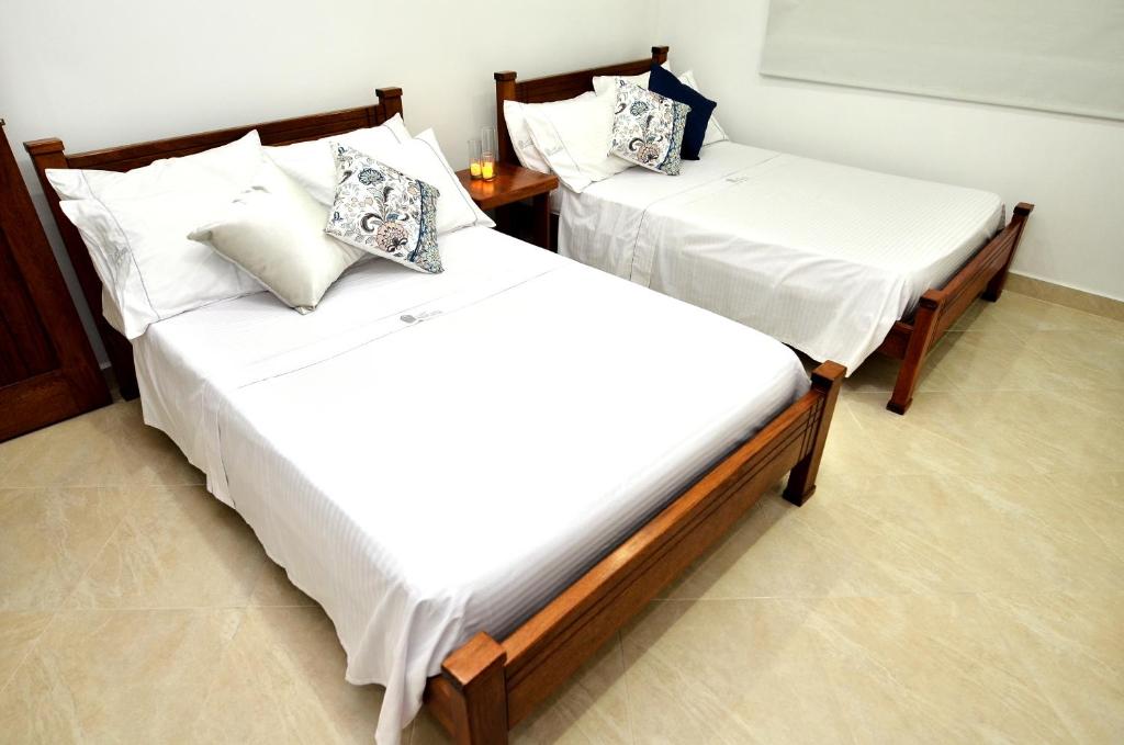 2 camas en una habitación con sábanas y almohadas blancas en Hotel La Gran Esquina, en Puerto Boyacá