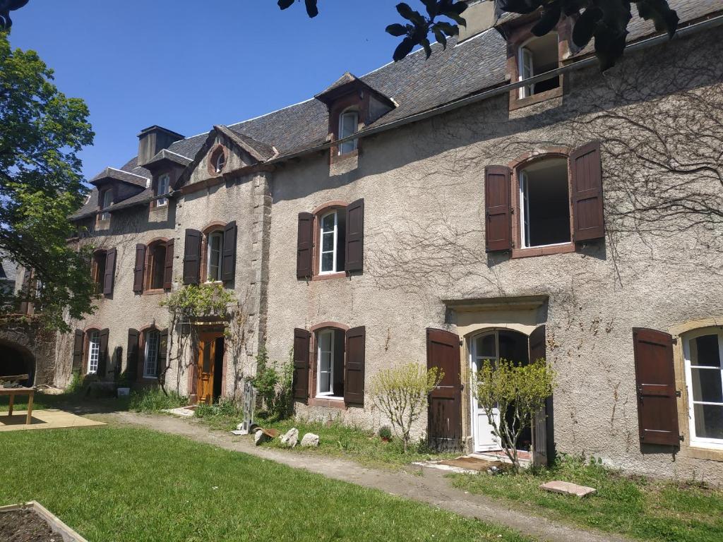 a large stone building with brown shutters and a yard at Chambres d'hôtes l'arche d'Yvann in Campuac