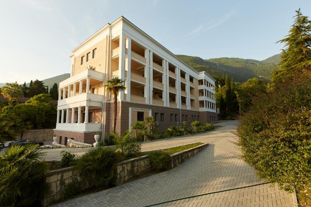 a large white building with a palm tree next to a road at Old Gagra Hotel in Gagra