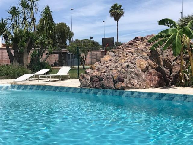 una piscina con 2 sillas y una pared de roca en Casa independiente con piscina y pista deportiva privadas, en El Puerto de Santa María