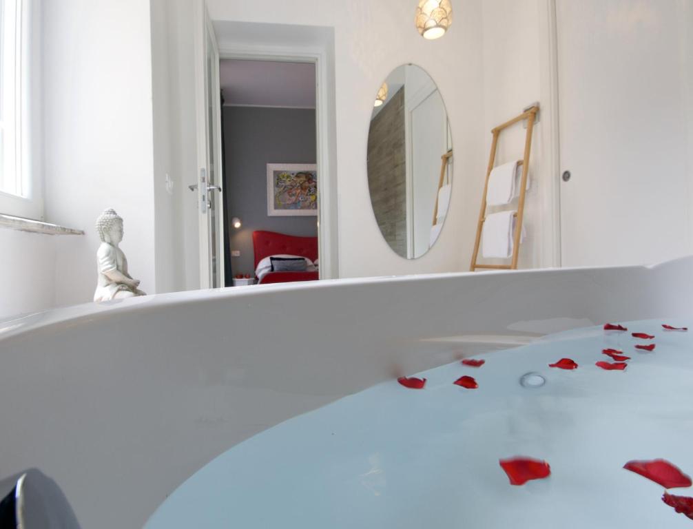 bagno con specchio e vasca con fiori rossi sul pavimento di B&B Amor a Roma