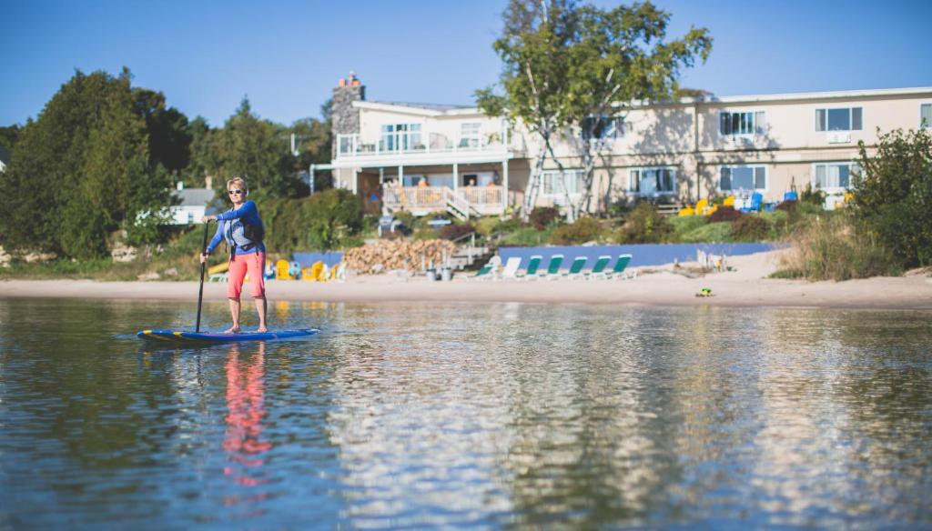 a man is standing on a paddle board in the water at Beachfront Inn in Baileys Harbor