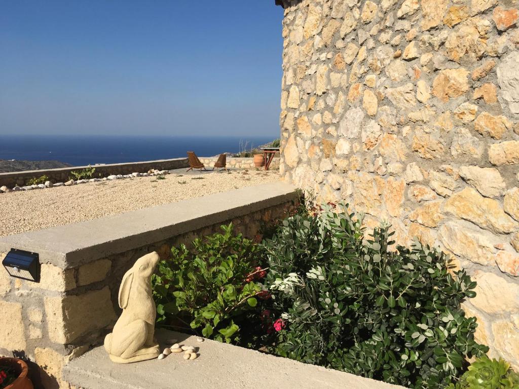 Una statua seduta su un cornicione accanto a un muro di pietra di Karpathos Guest House a Menetaí