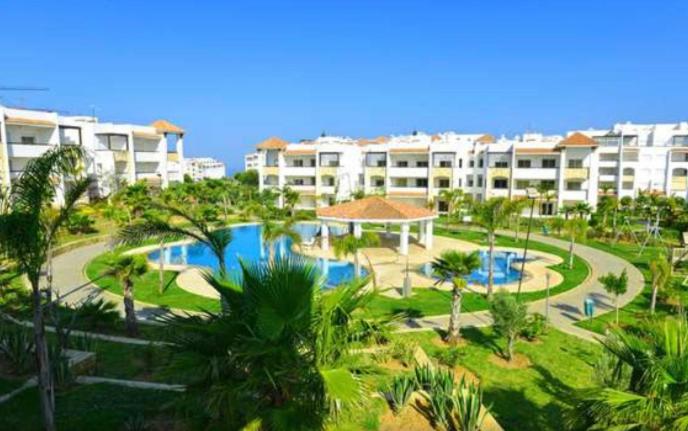 un complejo con piscina, palmeras y edificios en Assilah Marina Golf chez Ahmed, en Asilah