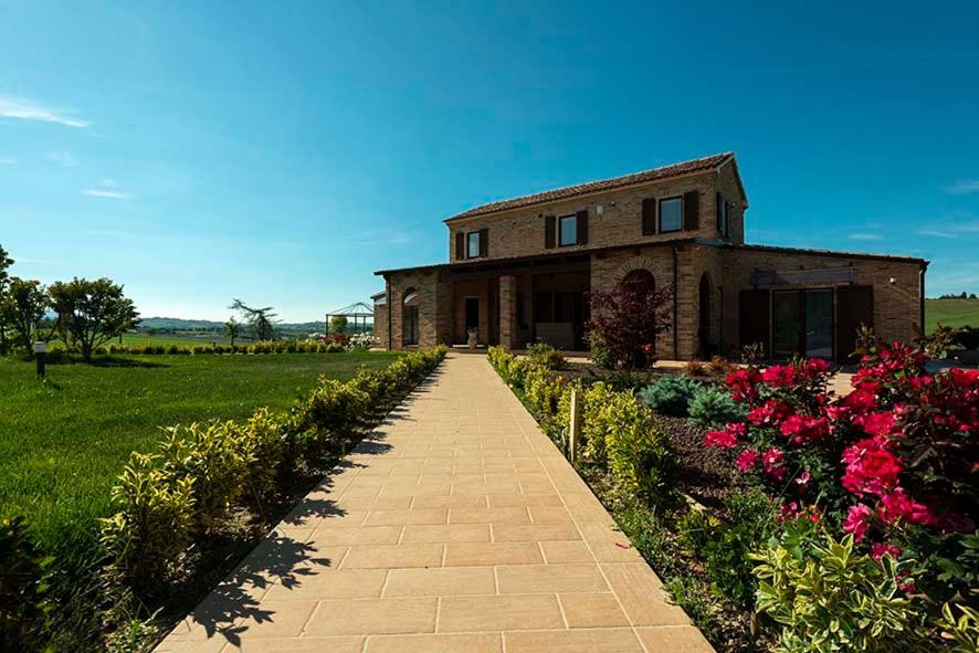 a brick house with a pathway in front of a field of flowers at B&B Olmo in Saludecio