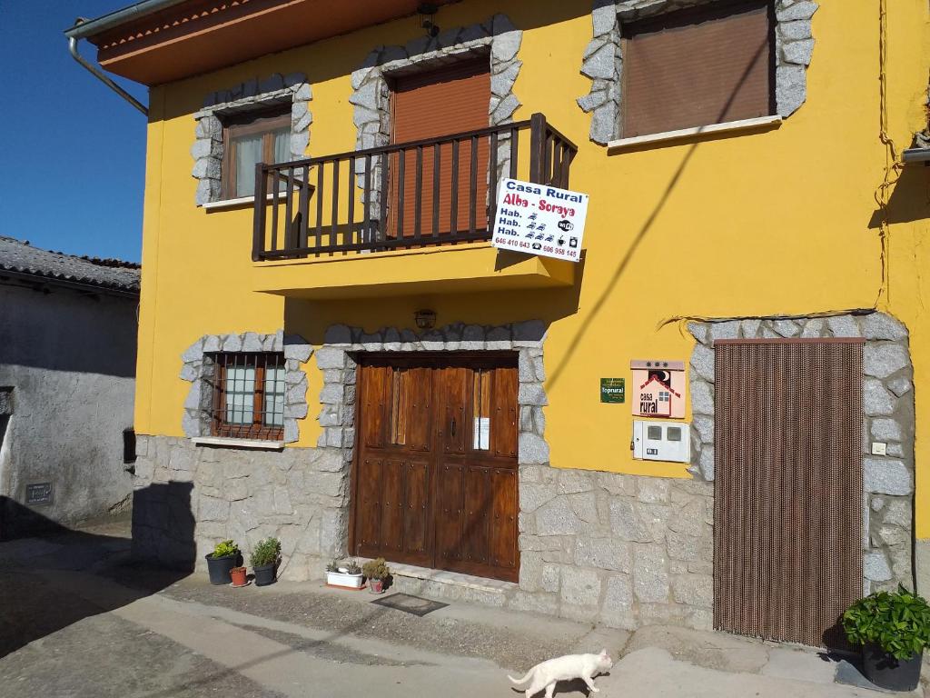 Una casa amarilla con un perro delante. en Alojamientos AlbaSoraya, en La Calzada de Béjar