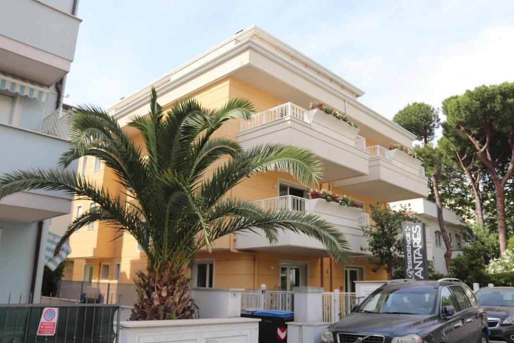 um edifício amarelo com uma palmeira em frente em Antares em Riccione