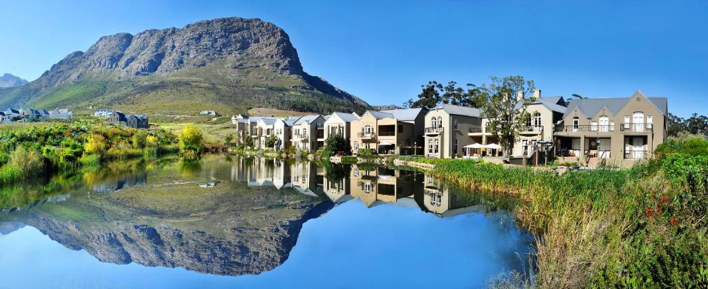 una fila de casas junto a un río con una montaña en L'ermitage - Franschhoek Chateau & Villas, en Franschhoek