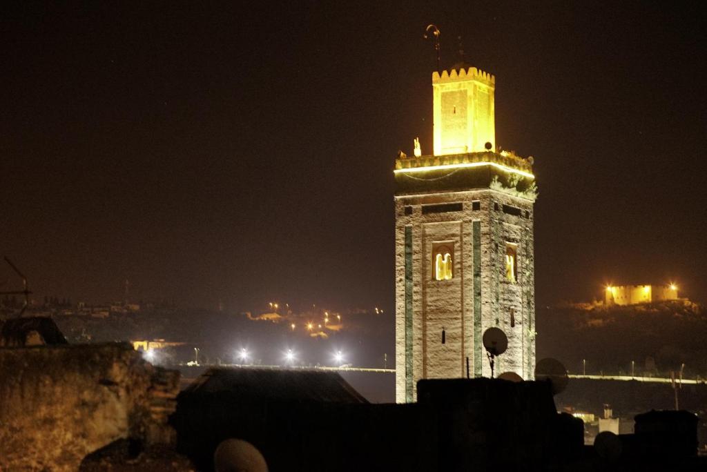 una torre del reloj alta con luces encendidas por la noche en Moroccan Dream Hostel, en Fez