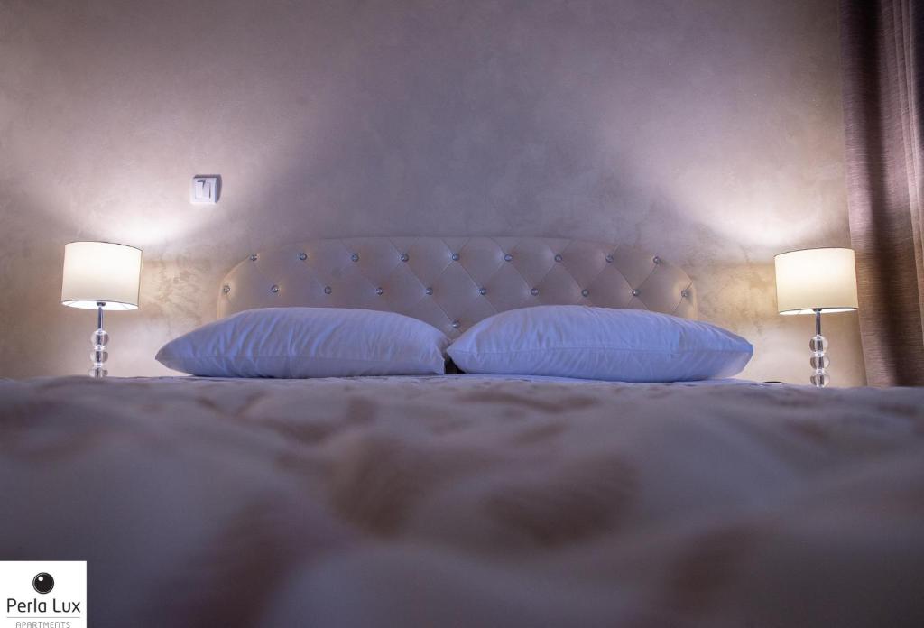 Perla Lux Apartments في أراندجيلوفاك: غرفة نوم بسرير ومخدات ومصباحين