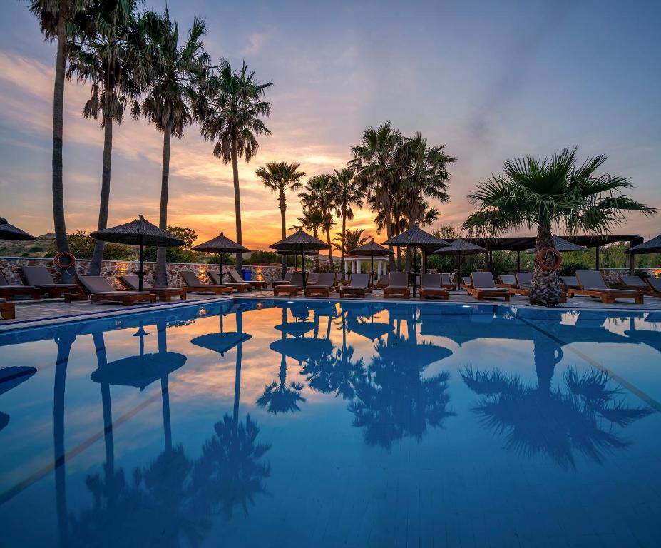 a swimming pool with chairs and umbrellas and palm trees at Argiri Resort Hotel & Apartments in Kardamaina