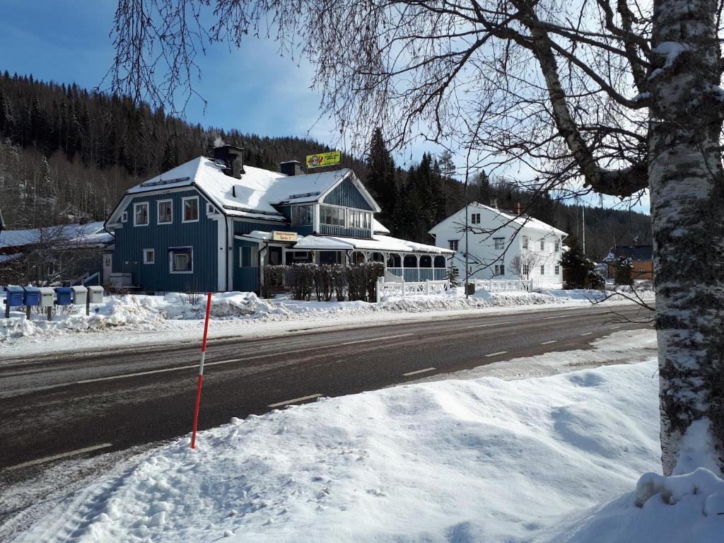 una casa azul al lado de un camino en la nieve en Wärdshuset Klarälvdalen en Sysslebäck