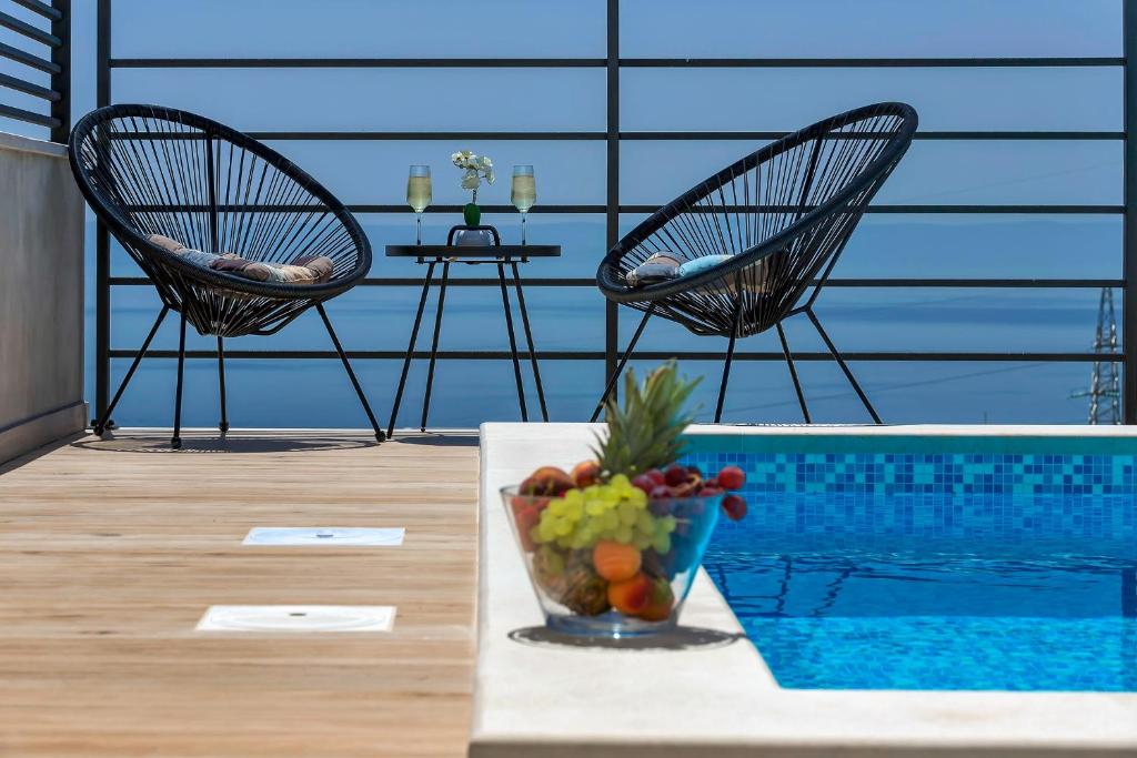 2 Stühle und ein Tisch mit einer Obstschale neben einem Pool in der Unterkunft Villa Violet with Salt water pool in Makarska