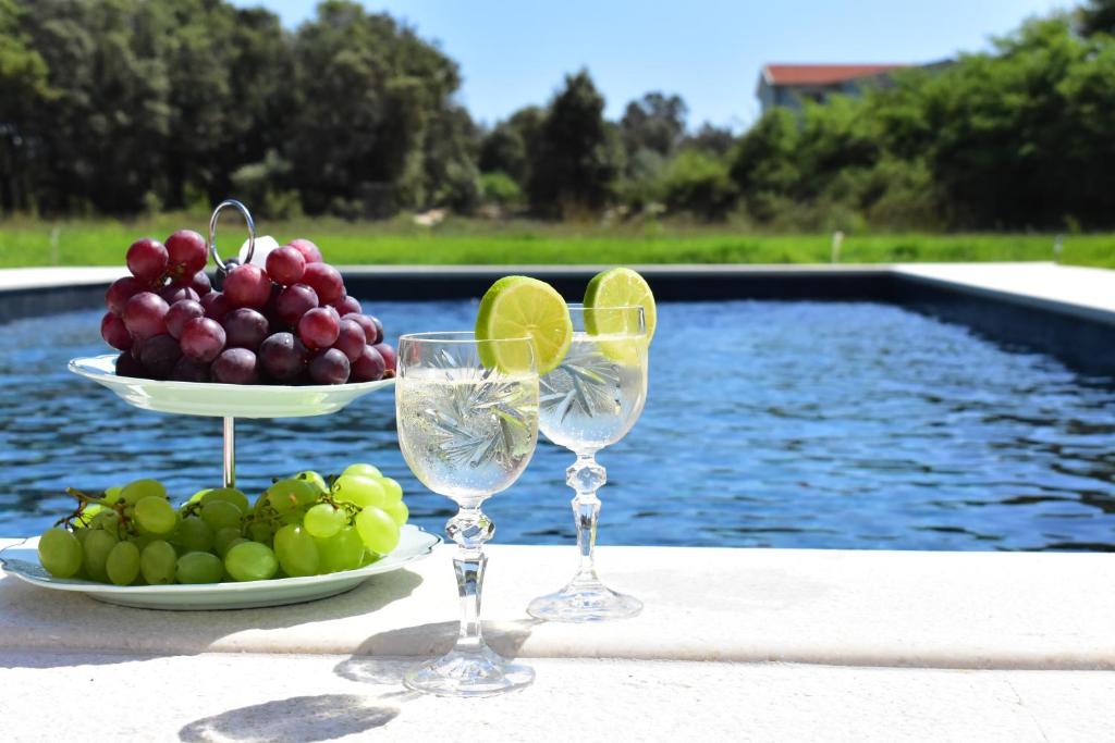 a plate of grapes and wine glasses next to a pool at Apartments Vesna in Zaton