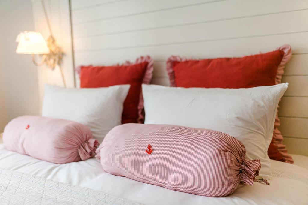 two pink pillows on a white bed with red pillows at Weißt Du noch - Gästehäuser & Suiten in Kühlungsborn