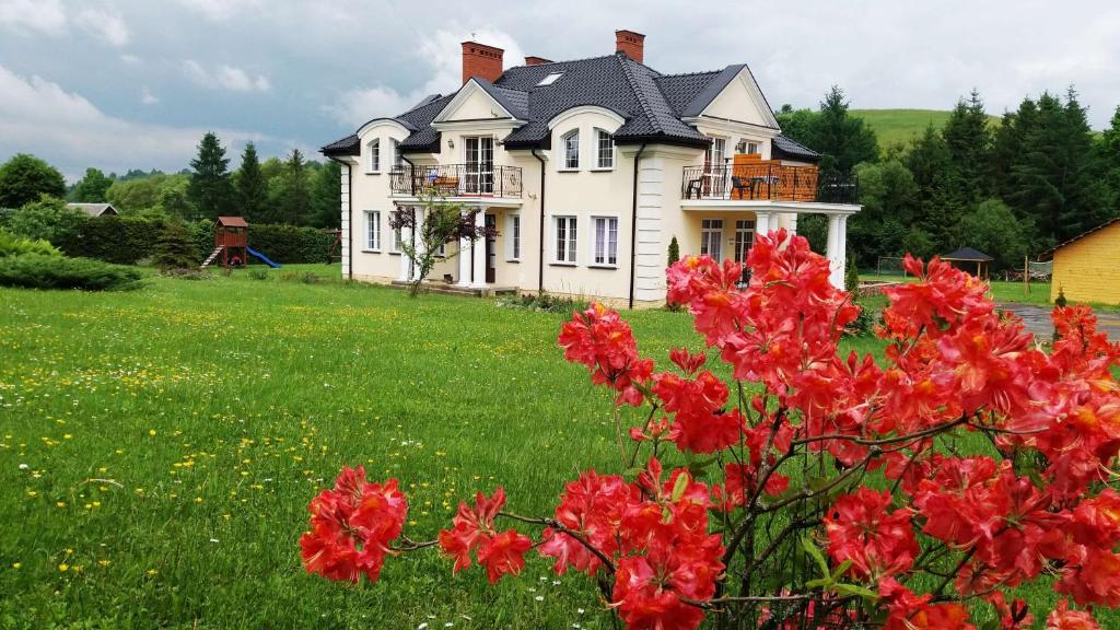 a large white house with red flowers in a field at Willa Kamieniec in Polańczyk