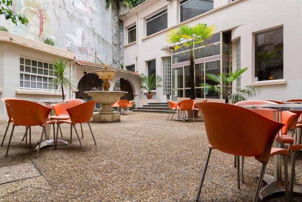un patio extérieur avec des tables, des chaises et une fontaine dans l'établissement The Originals City, Hôtel Astoria Vatican, Lourdes (Inter-Hotel), à Lourdes