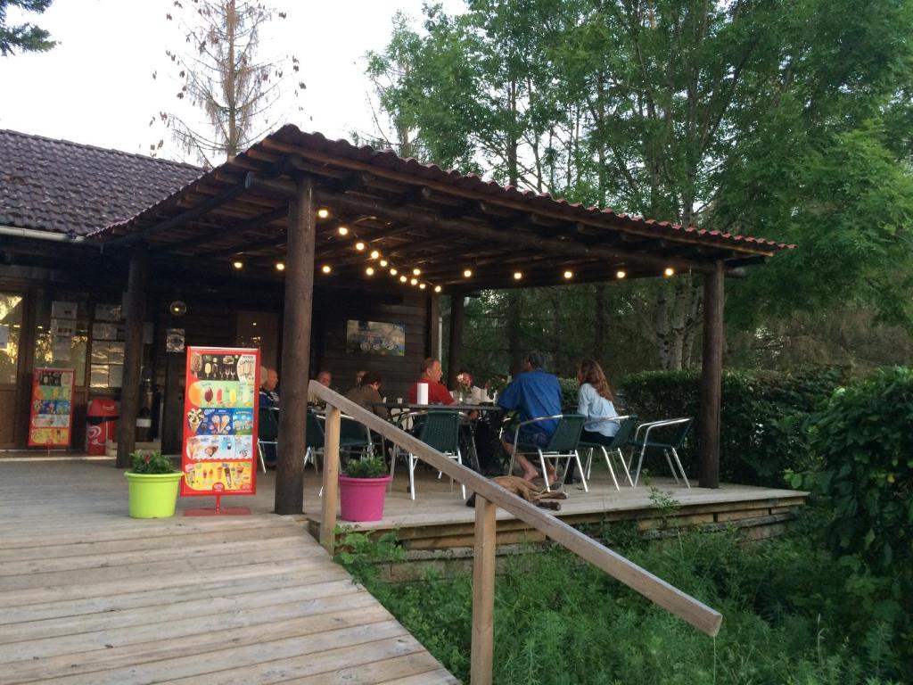 a wooden pergola with people sitting at tables on a deck at Camping Le Canoë in Chaussin