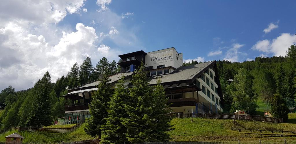 un grand bâtiment au sommet d'une colline plantée d'arbres dans l'établissement Kinder- und Familienhotel Nockalm, à Innerkrems