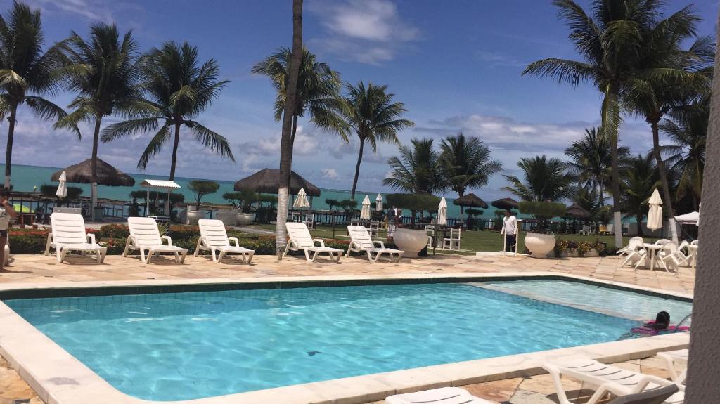 uma piscina num resort com cadeiras e palmeiras em Flats apart hotel marinas Carneiros - vista p mar em Tamandaré