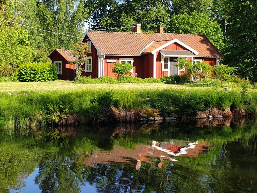 une maison rouge à côté d'une rivière arborée dans l'établissement WESTERQVARN, à Mölntorp