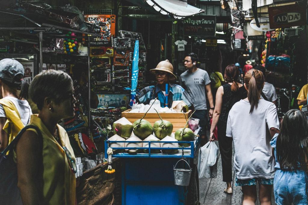 a man standing in a market with a cart full of coconuts at Luk Hostel in Bangkok