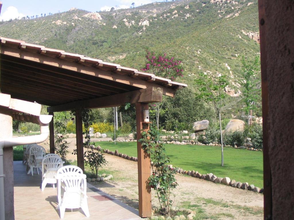 a wooden pergola with white chairs and a lawn at l'Ogliastru in Ucciani