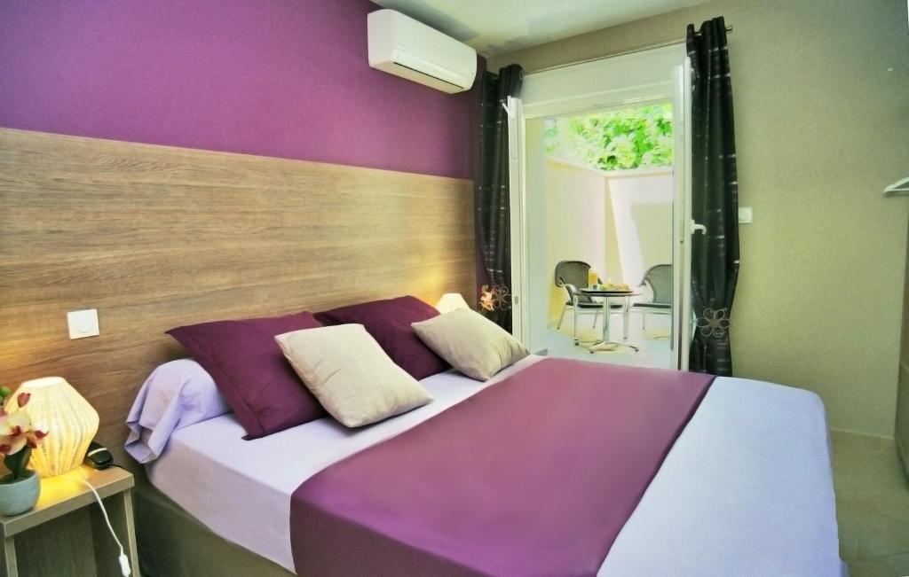 ein lila und weißes Bett in einem Zimmer in der Unterkunft Hôtel l'Anvia in Bollène