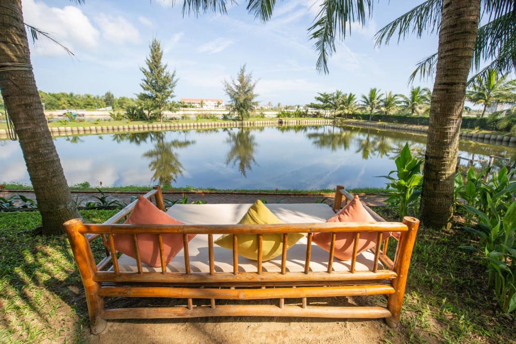 a bed in front of a lake with palm trees at Tra Que Mansion in Hoi An