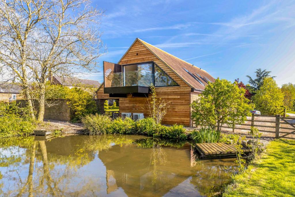 una casa de madera con un estanque frente a ella en The Loft : Luxury Countryside Retreat for Family & Friends, en Clipston