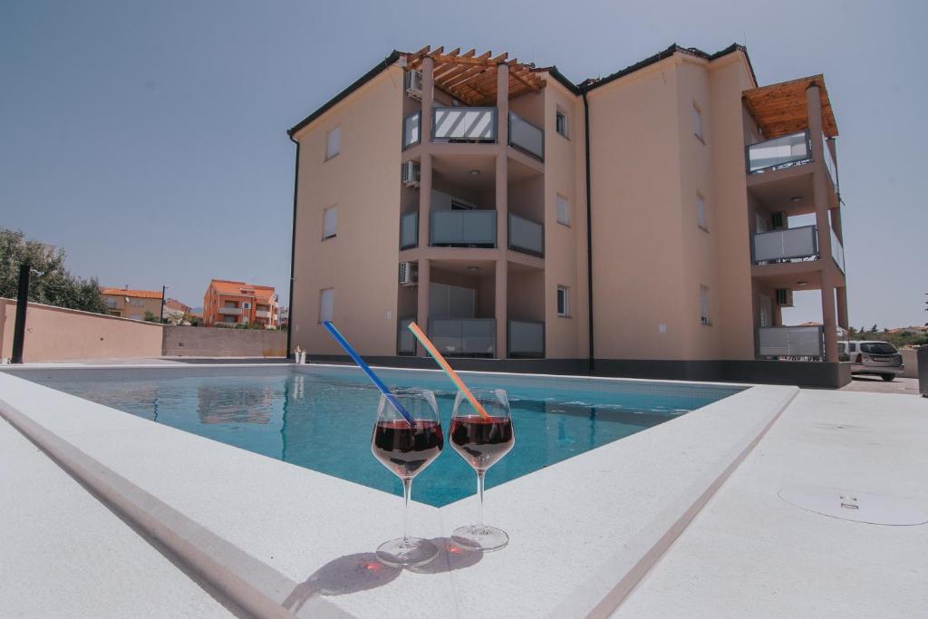 two glasses of wine sitting on a ledge next to a swimming pool at Poolside Hideout Apartments in Novalja