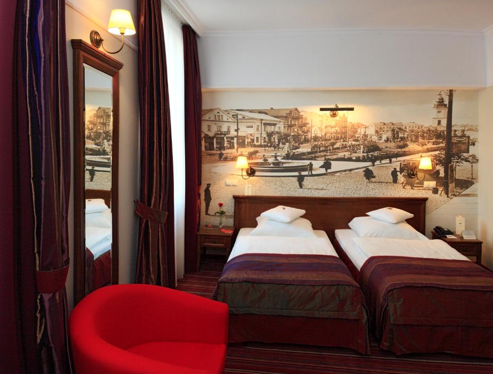 ビャウィストクにあるBranicki Boutique Roomsのベッド2台と赤い椅子が備わるホテルルームです。