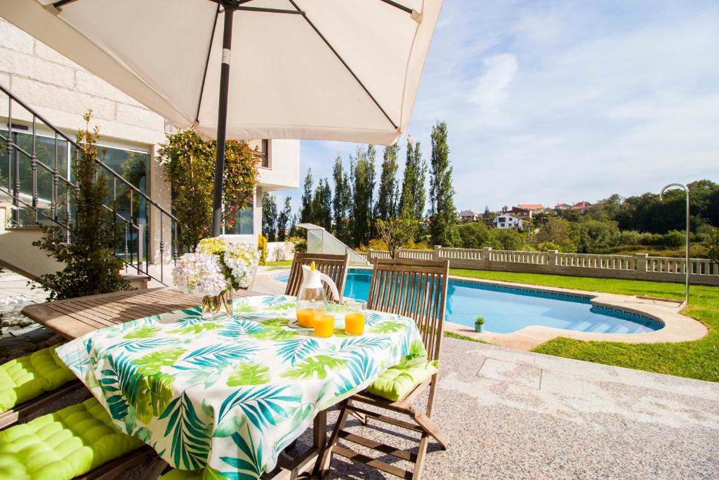 uma mesa e cadeiras com um guarda-sol ao lado de uma piscina em Villa El Castañal con Piscina Privada em Vigo