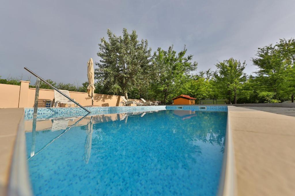 a large blue swimming pool with a umbrella and trees at Mobile Home Grbe in Nin