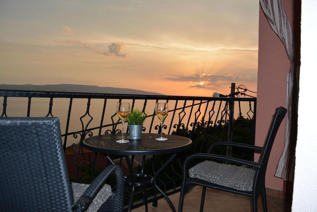 a table and chairs on a balcony with a sunset at Apartments & Room MaDi in Senj