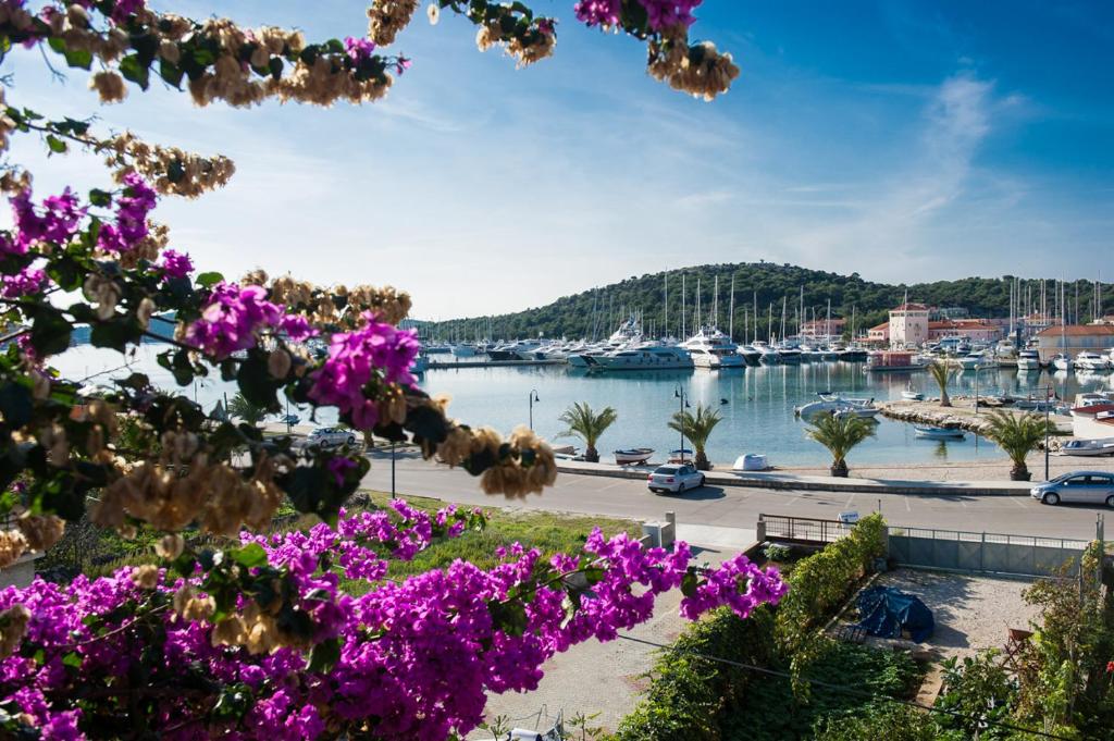 a marina with boats in the water and purple flowers at Apartments Bilja - 20 M from the sea in Rogoznica