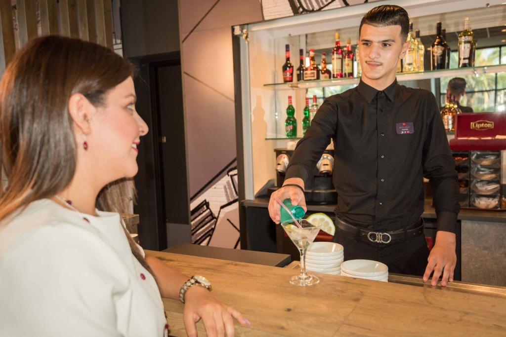 a woman standing at a bar with a man preparing a drink at ibis Alger Aéroport in Alger