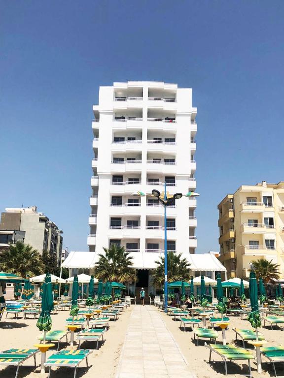 Una playa con sillas y un gran edificio blanco. en Perandor Beach, en Durrës