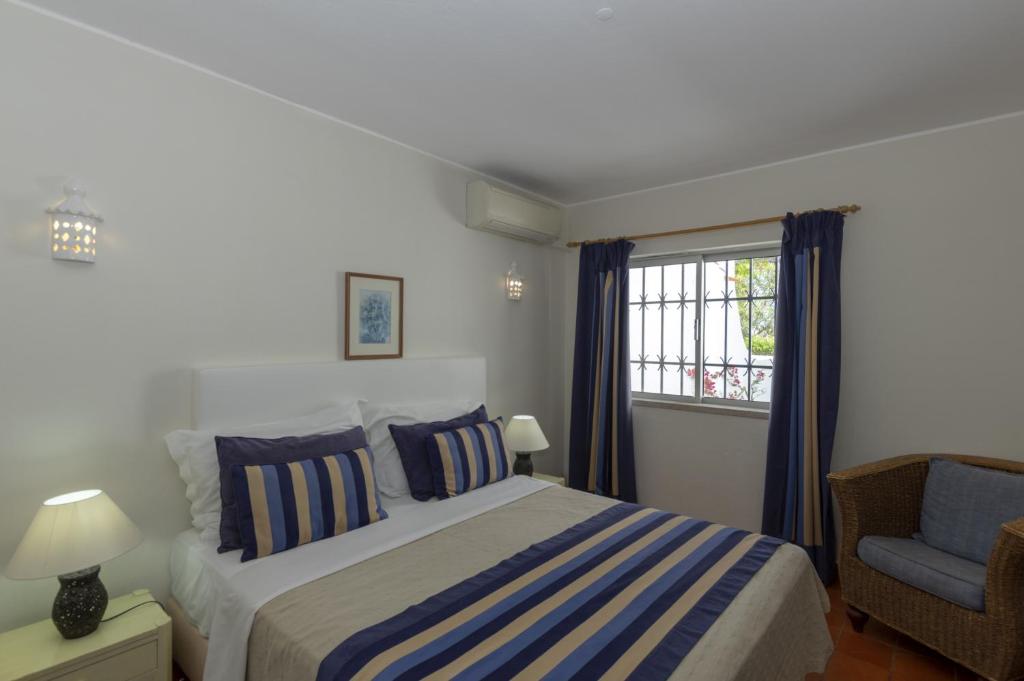a bedroom with a bed and a chair and a window at Rocha Brava Village Resort in Carvoeiro