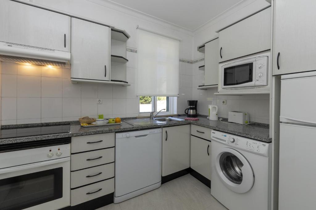 a kitchen with white cabinets and a washer and dryer at Rocha Brava Village Resort in Carvoeiro