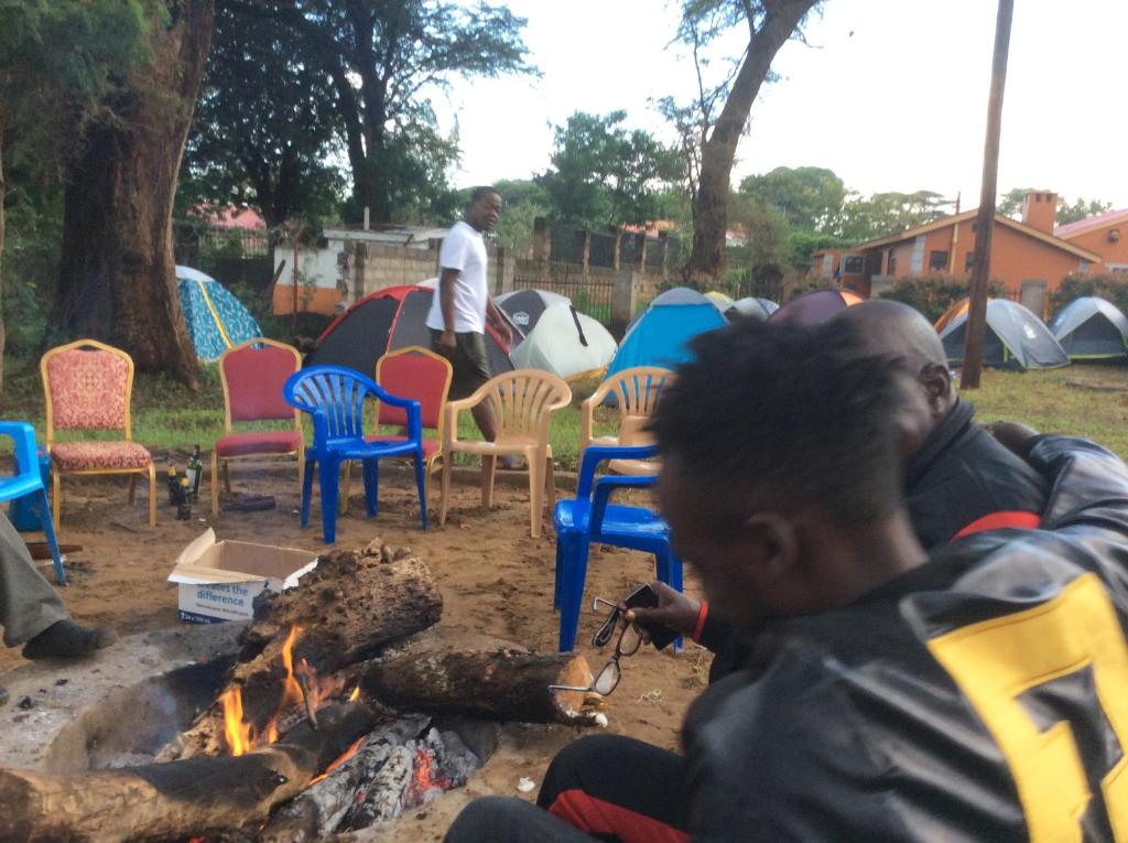 a man sitting next to a fire with chairs and tents at Tita Tourist Resort in Moroto