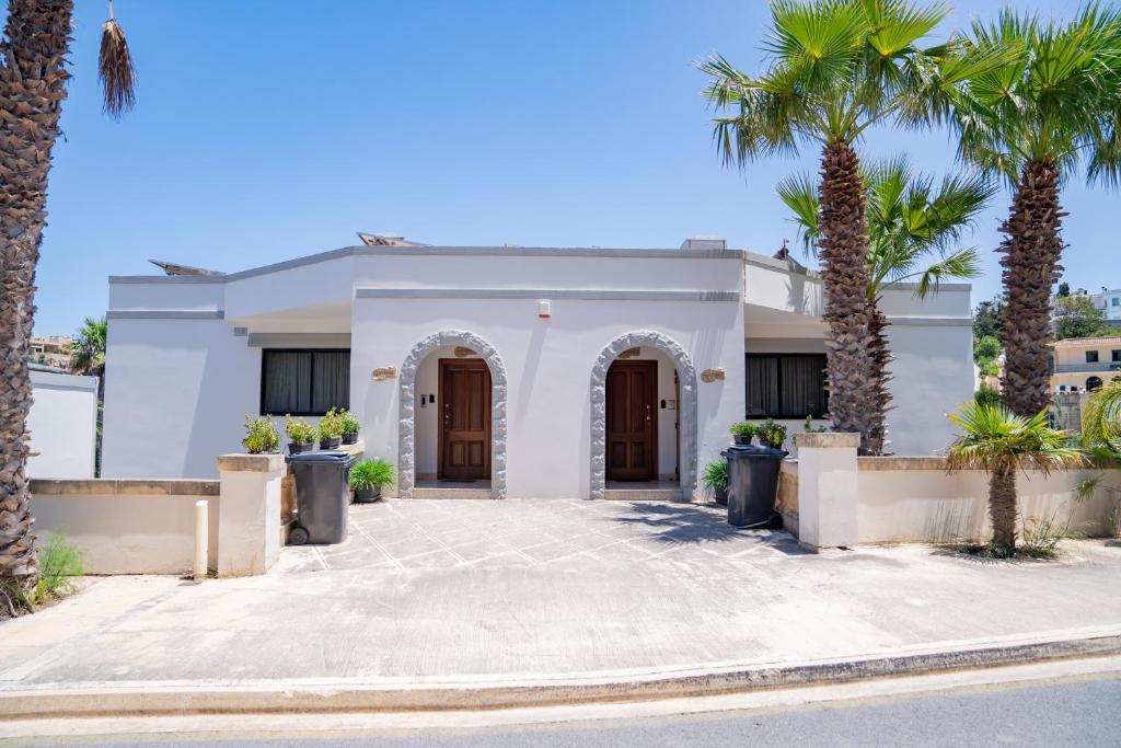 a white house with palm trees in front of it at Baldacchino Holiday Villas in Mellieħa