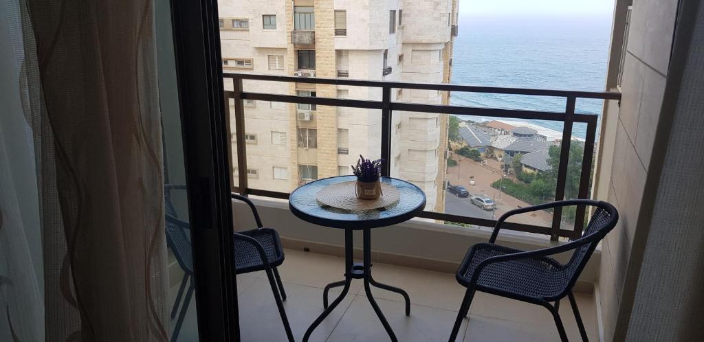 een tafel en stoelen op een balkon met uitzicht op de oceaan bij 2 BDR Nitza appartment with balkony in Netanya