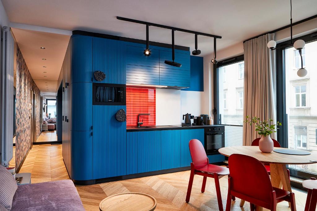 a blue kitchen with a table and red chairs at Rajska Blue Luxury Apartment in Kraków