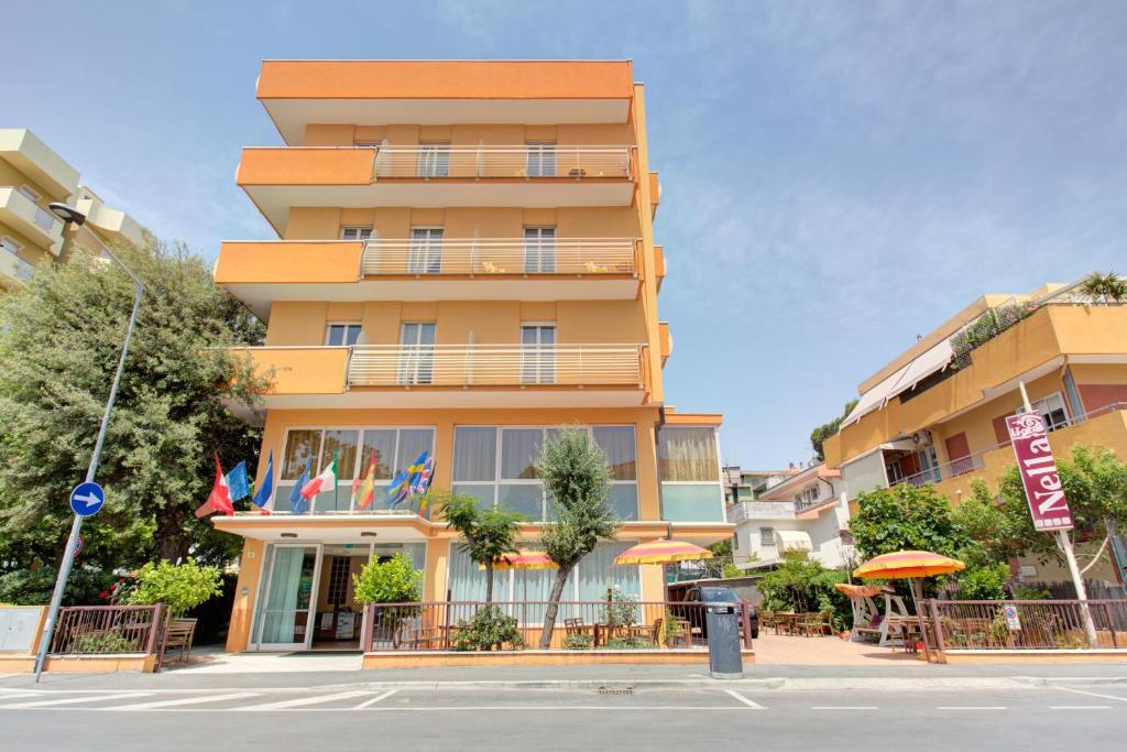 un grand bâtiment jaune avec des drapeaux devant lui dans l'établissement Hotel Nella, à Rimini