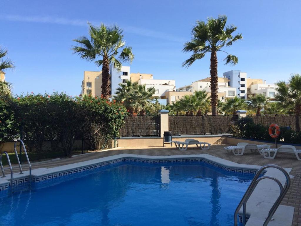 a swimming pool with palm trees and buildings in the background at Beach Apartment in Huelva