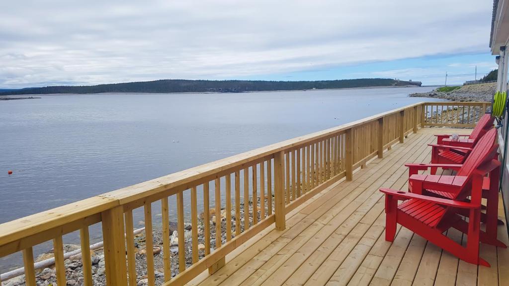 three red chairs sitting on a deck overlooking the water at A Wave From it All in Port Saunders