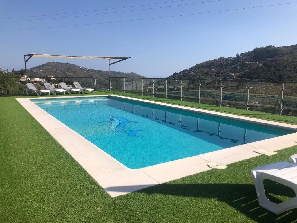 Una piscina con césped verde y montañas al fondo. en Casa Olivia, en Cómpeta