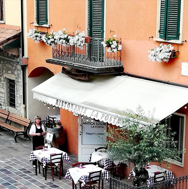a woman standing outside of a restaurant with tables and chairs at Antica Locanda La Posta in Gaggio Montano