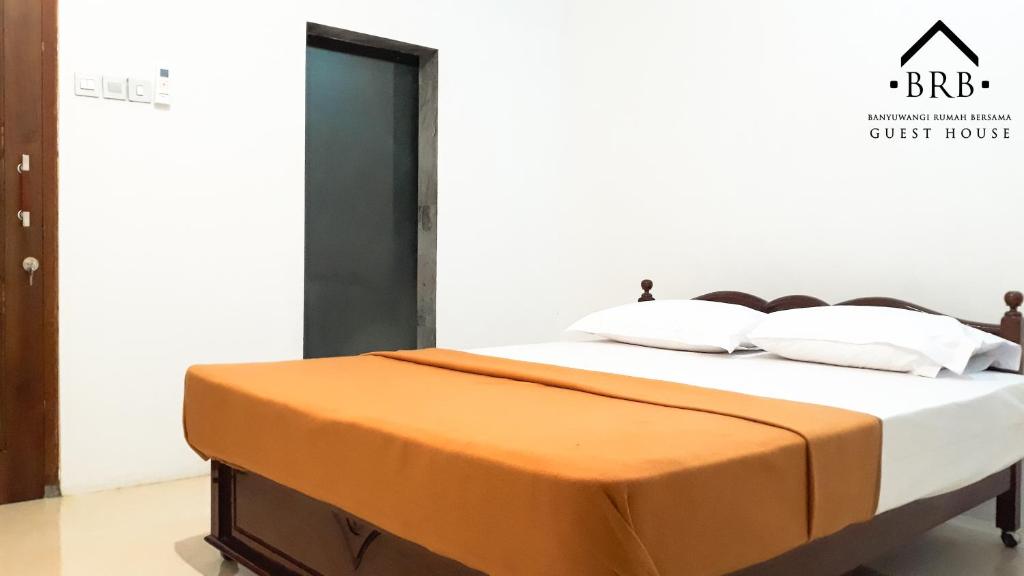 a bed with an orange blanket on top of it at BRB Guesthouse in Banyuwangi